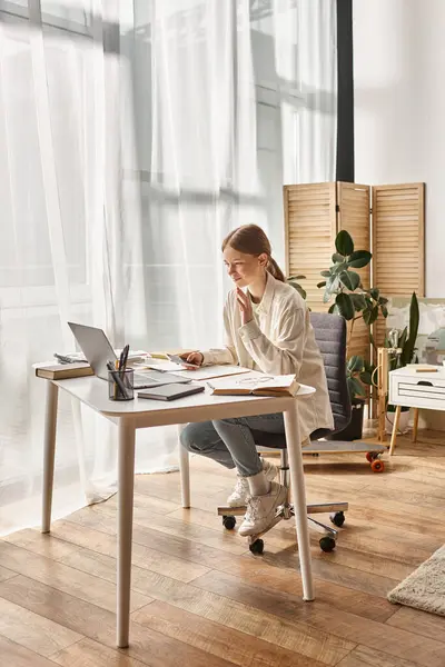 Cheerful teenage girl using her laptop while sitting around books, online education concept — Stock Photo