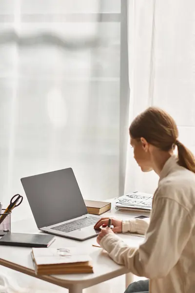 Adolescente usando su computadora portátil y tomando notas mientras está sentada alrededor de libros, concepto de educación en línea - foto de stock