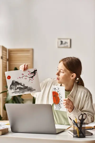 Adolescente montrant ses œuvres tout en étudiant et en regardant son ordinateur portable, classe d'art en ligne — Photo de stock