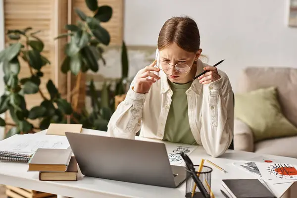 Adolescent fille parler sur smartphone et regarder ordinateur portable près de son croquis dessin sur le bureau — Photo de stock