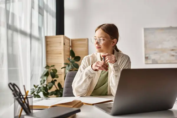 Teenager mit Brille hält Stift in der Hand und denkt während des Online-Unterrichts am Laptop und macht sich Notizen — Stockfoto