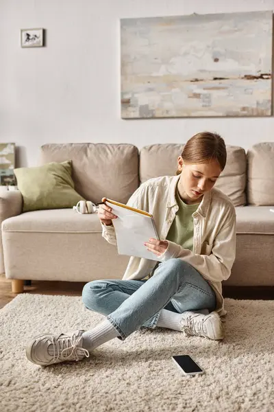 Teenage girl holding her notebook near the couch with headphones and looking at smartphone — Stock Photo
