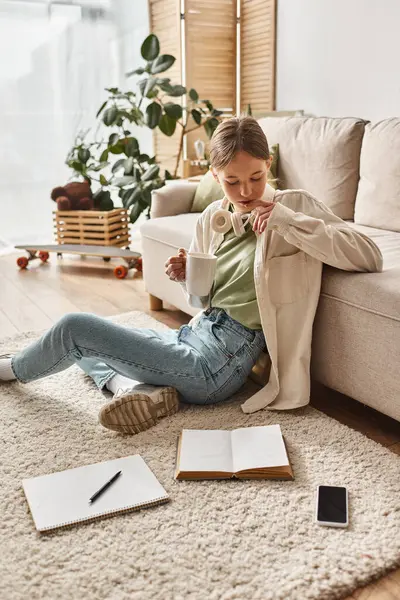 Teenie-Mädchen mit Kopfhörern genießt Kaffee zu Hause und schaut auf Teppich auf Smartphone und Notebook — Stockfoto