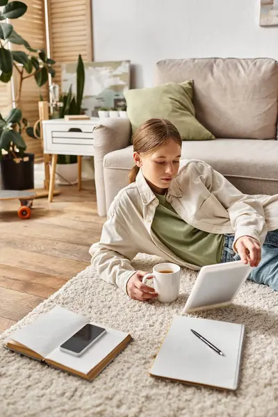Adolescente segurando tablet e xícara de chá ao fazer seu dever de casa, conceito nativo digital — Fotografia de Stock
