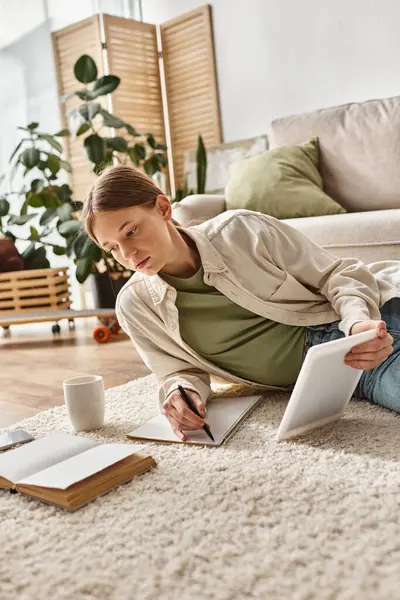 Teenager girl holding tablet and taking notes while making her homework, digital native concept — Stock Photo