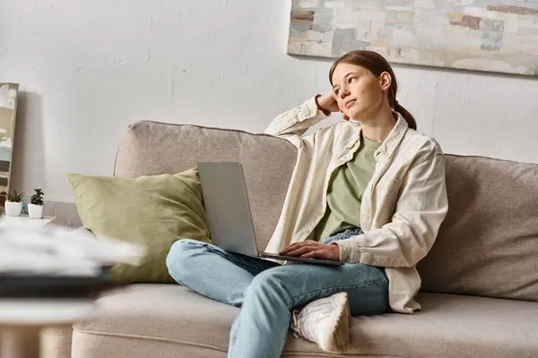 Ragazza adolescente sognante seduta con il suo computer portatile su un comodo divano a casa, concetto di apprendimento a distanza — Foto stock