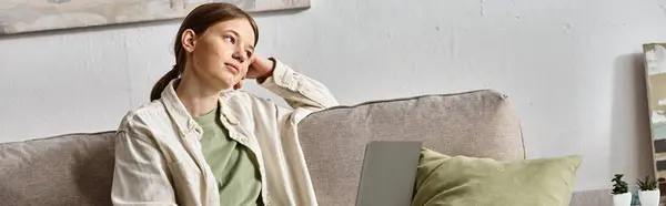 Bandera de la muchacha adolescente soñadora que se sienta con su computadora portátil en un sofá en el hogar, concepto de e-learning - foto de stock