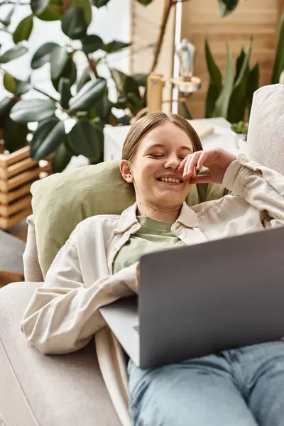 Heureuse adolescente en utilisant son ordinateur portable et couché sur un canapé confortable à la maison, enseignement à distance — Photo de stock