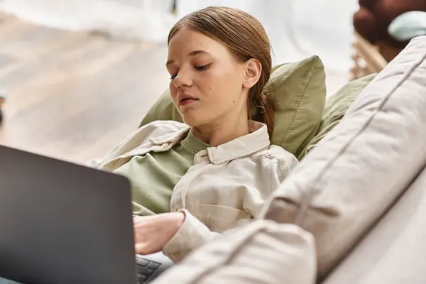 Adolescente centrada en e-learning usando su portátil y acostada en un cómodo sofá en casa - foto de stock