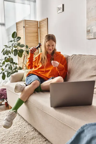 Emotional teen girl with joystick and laptop losing game and sitting on sofa at home, weekend vibes — Stock Photo