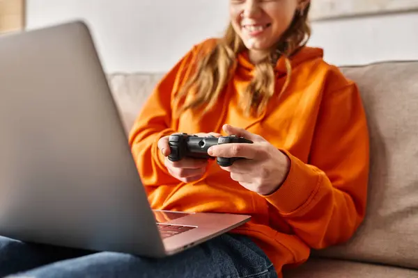 Zugeschnittene Teenager-Mädchen, die mit Steuerknüppel und Laptop spielen, während sie zu Hause auf dem Sofa sitzen, Wochenendstimmung — Stockfoto