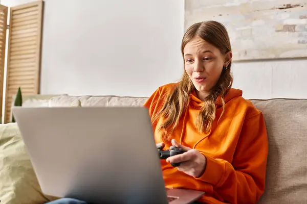 Jeu adolescent étonnant fille avec joystick et ordinateur portable tout en étant assis sur le canapé à la maison, vibes week-end — Photo de stock