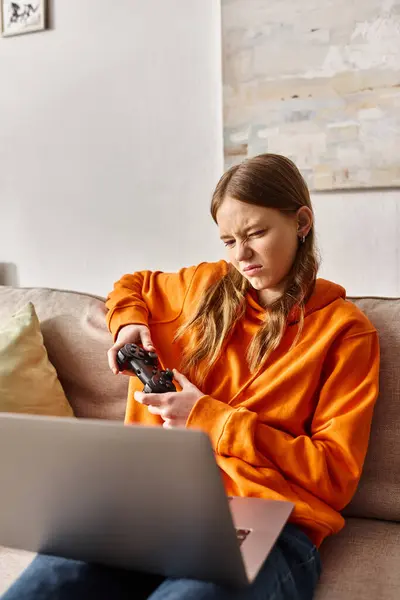 Displeased teenage girl gaming with joystick and laptop while sitting on sofa at home, entertainment — Stock Photo
