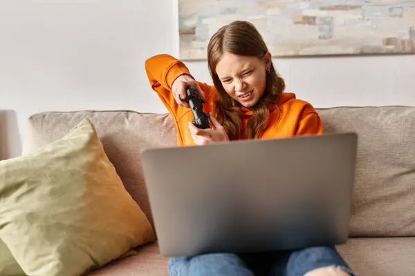 Adolescent tendu jeu de fille avec joystick et ordinateur portable et assis sur le canapé à la maison, divertissement — Photo de stock