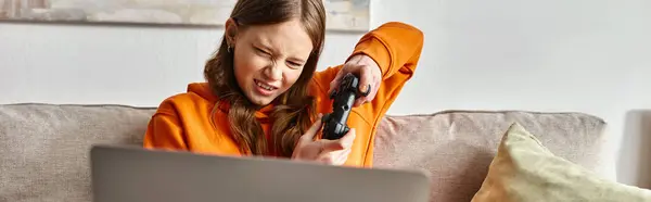 Adolescent tendu jeu de fille avec joystick et ordinateur portable et assis sur le canapé à la maison, bannière — Photo de stock