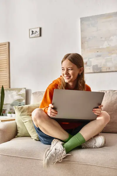Веселая девочка-подросток с ноутбуком, наслаждающаяся временем и сидящая на диване в гостиной — стоковое фото