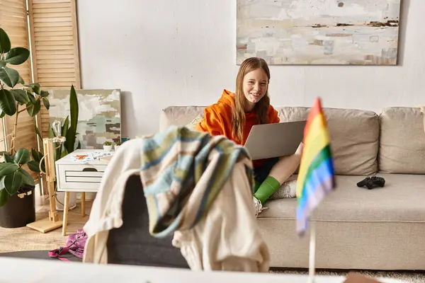 Focus sur adolescent fille assis avec son ordinateur portable près flou lgbt drapeau arc-en-ciel sur le bureau, identité — Photo de stock