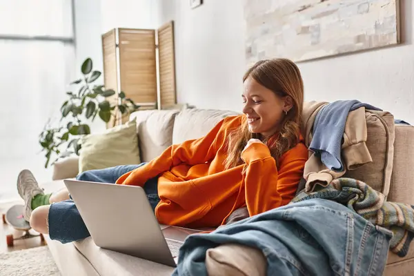 Щаслива дівчина-підліток дивиться фільм на ноутбуці, розслабляючись на дивані у вітальні, дозвілля — стокове фото