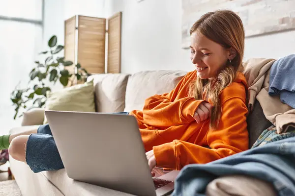 Щаслива дівчина-підліток дивиться комедійний фільм на ноутбуці, розслабляючись на дивані у вітальні — стокове фото