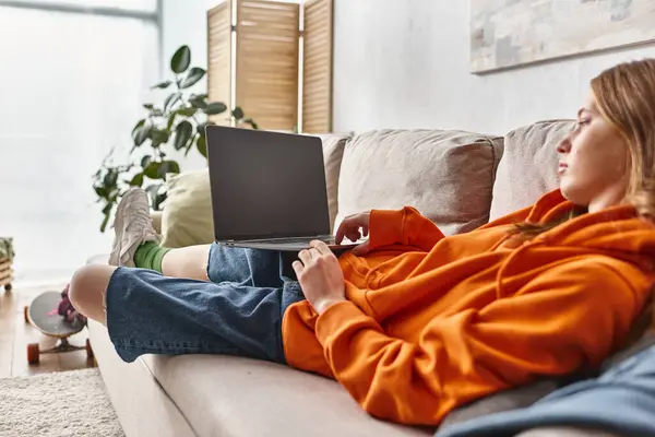 Adolescent fille regarder film sur un ordinateur portable avec écran blanc tout en se relaxant sur un canapé dans le salon — Photo de stock