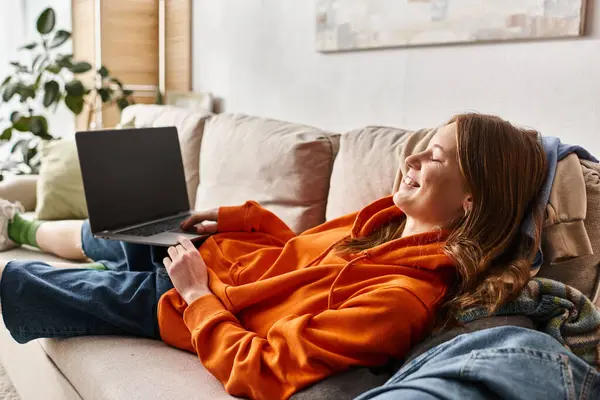 Felice adolescente ragazza guardando film commedia su un computer portatile con schermo bianco mentre si rilassa su un divano — Foto stock