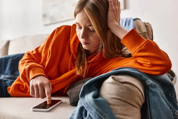 Troubled teenage girl browsing her smartphone and feeling down while resting on the sofa — Stock Photo