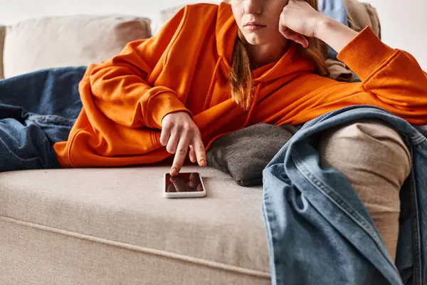 Recortado problemático adolescente navegar por su teléfono inteligente y sentirse abajo mientras descansa en el sofá - foto de stock