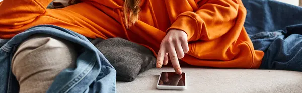 Обрізаний банер дівчини-підлітка, що переглядає свій смартфон і відчуває себе вниз, відпочиваючи на дивані — стокове фото