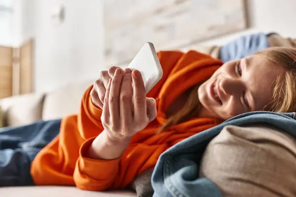 Cheerful teenage girl using her smartphone and sitting on sofa in living room, social media user — Stock Photo