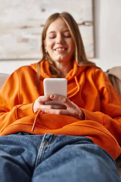 Happy teenage girl using her smartphone and sitting on sofa in living room, social media user — Stock Photo