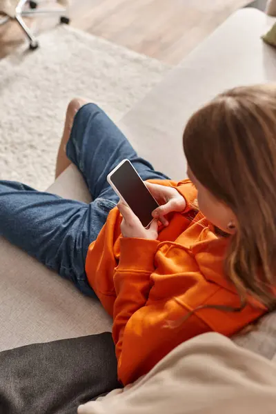 Zoomer teenager girl using her smartphone and sitting on sofa in living room, social media user — Stock Photo