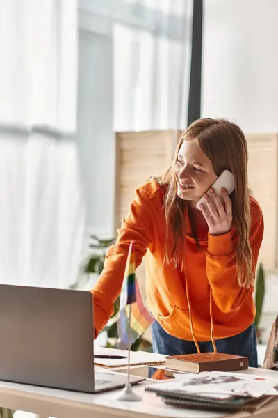Smiling teenager girl studying online at home, making a call next to pride lgbtq flag on desk — Stock Photo