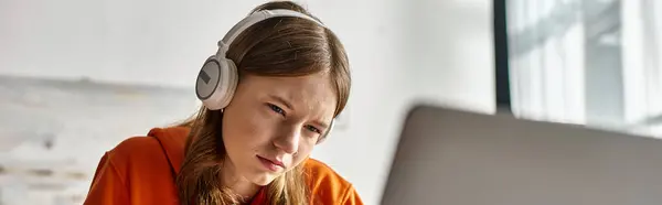 Joven adolescente enfocada en auriculares inalámbricos e-learning con computadora portátil en casa, bandera horizontal - foto de stock