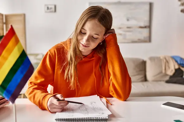 Smiling teenage girl drawing a sketch, immersed in creative process with pride flag beside her — Stock Photo