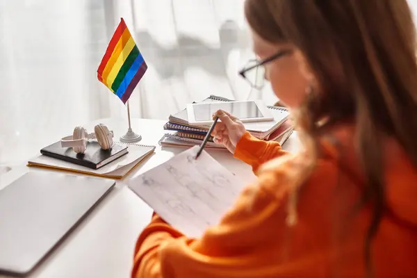 Blurred teenage girl drawing a sketch, immersed in creative process with pride flag beside her — Stock Photo