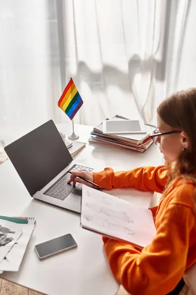 Adolescent fille dans lunettes dessin croquis et en utilisant son ordinateur portable près drapeau de fierté et gadgets sur le bureau, art — Photo de stock