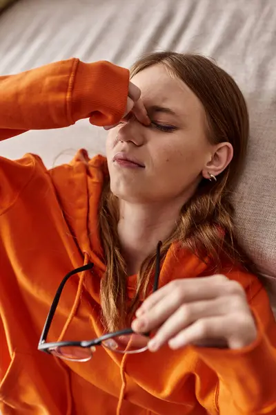 Vista dall'alto della stanca ragazza adolescente con cappuccio arancione appoggiata sul divano di casa, malinconia e solitudine — Foto stock