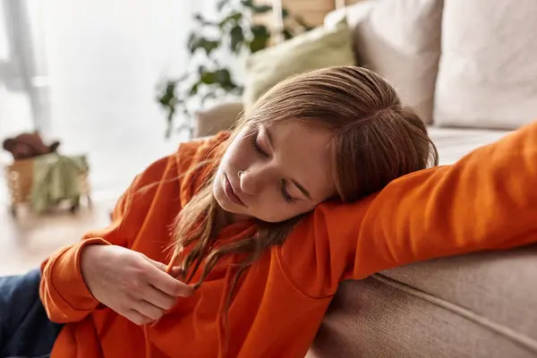 Chateado adolescente menina em laranja com capuz encostado no sofá em um ambiente acolhedor casa, solidão e tristeza — Fotografia de Stock