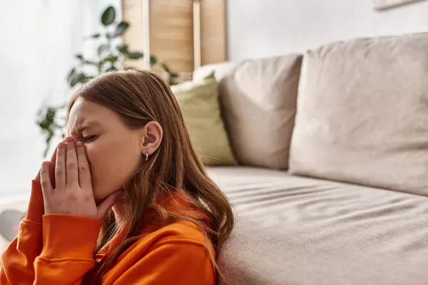 Teenage girl in distress, covering face with hands while crying near couch in living room — Stock Photo