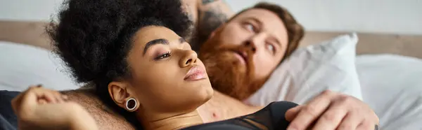 Young and curly african american woman in lingerie lying next to her man in bedroom, banner — Stock Photo