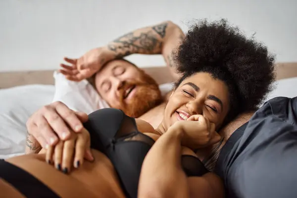 Happy and curly african american woman in lingerie lying next to her man in bedroom, soulmates — Stock Photo