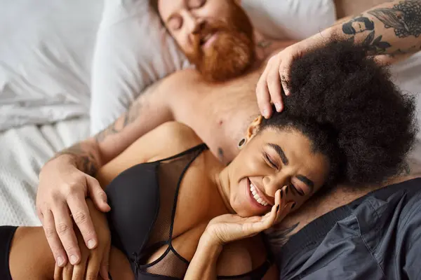 Souriante et frisée afro-américaine en lingerie couchée à côté de son homme dans la chambre, âmes sœurs — Photo de stock