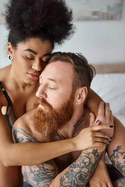Casal diversificado, mulher americana africana sensual abraçando seu homem tatuado em uma cama em um quarto brilhante — Fotografia de Stock