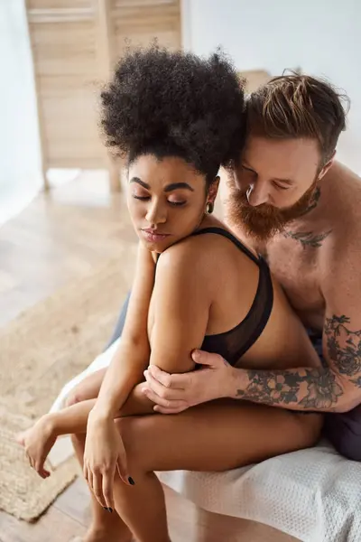 Разнообразная пара, бородатый мужчина с татуировками и африканская американская женщина, разделяющая нежный момент в постели — стоковое фото