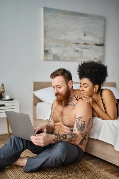 Homme tatoué barbu et femme afro-américaine regardant un film sur ordinateur portable, couple multiculturel — Photo de stock