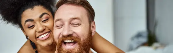 Tattooed and bearded man laughing with african american woman together at home, horizontal banner — Stock Photo
