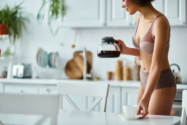 Donna afroamericana ritagliata e felice con toppe per gli occhi in possesso di tazza e caffettiera in cucina — Foto stock