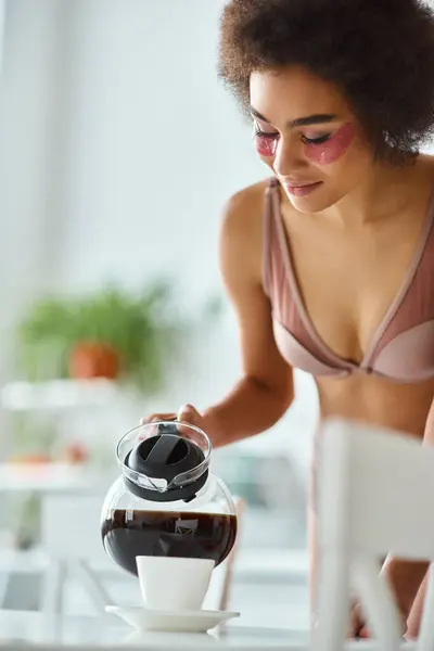 Feliz joven afroamericana mujer con parches para los ojos vertiendo café en taza de porcelana en la cocina - foto de stock