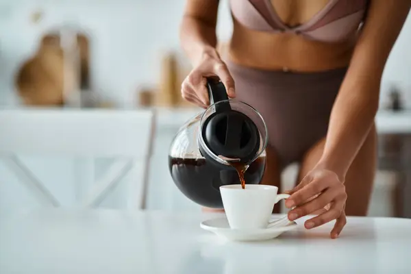 Cropped view of african american woman in underwear pouring coffee into porcelain cup in kitchen — Stock Photo