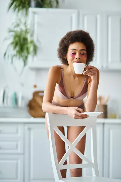 Happy african american woman with eye patches standing in underwear and smelling morning coffee — Stock Photo